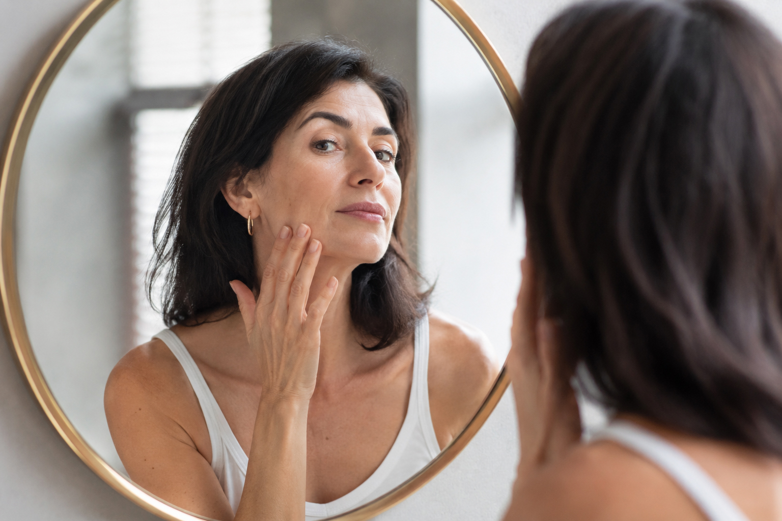 Woman examining facial volume and contours in a mirror before dermal filler treatment